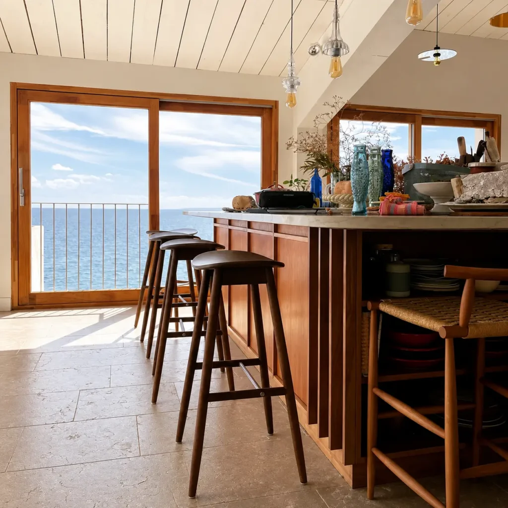 Cuisine moderne sur-mesure avec îlot central en bois, tabourets et vue panoramique sur la mer, une conception de l'ébéniste Rodolphe Castellani dans le Var.